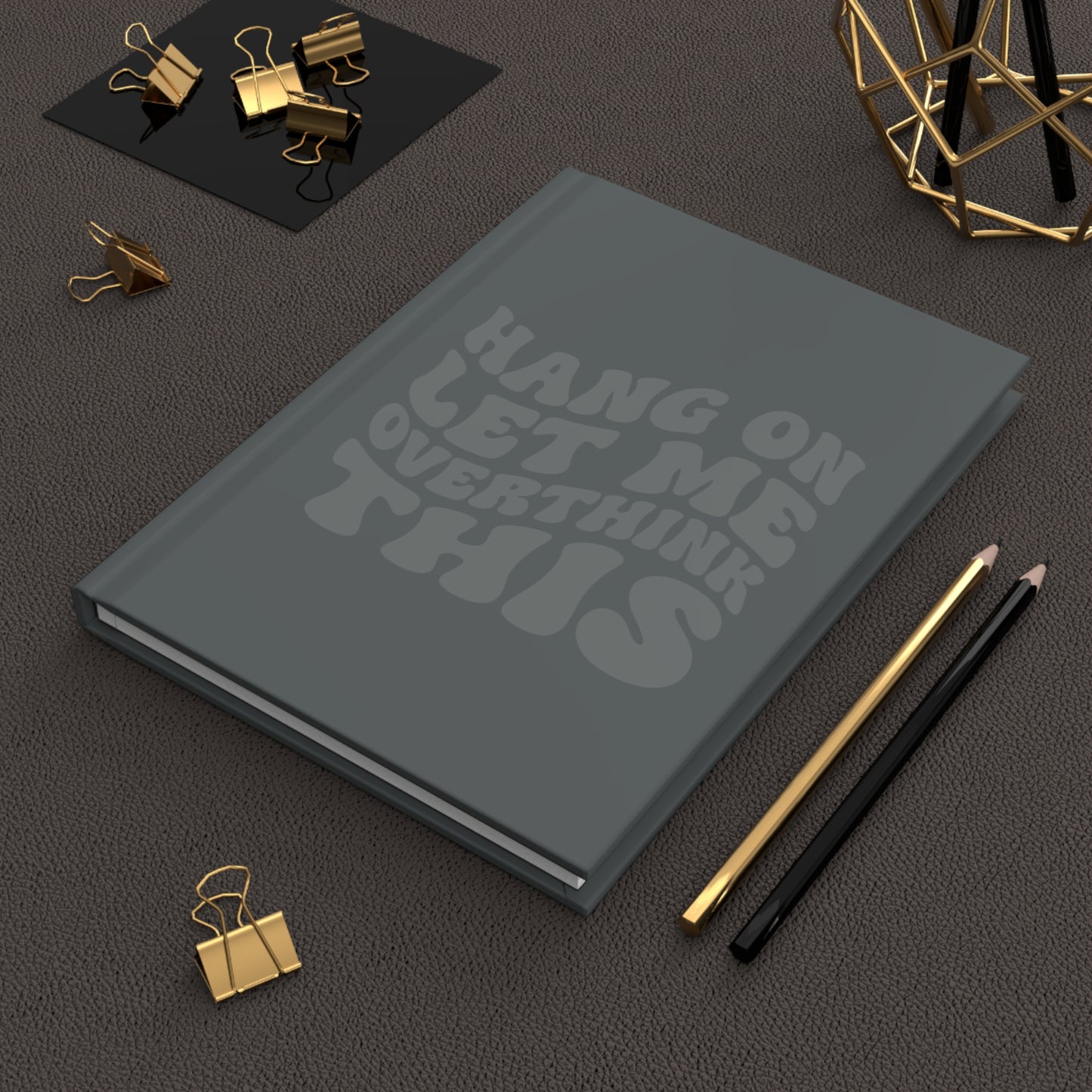 Gray hardcover journal with dark gray retro-style text that reads “Hang On Let Me Overthink This” in a monochrome design.