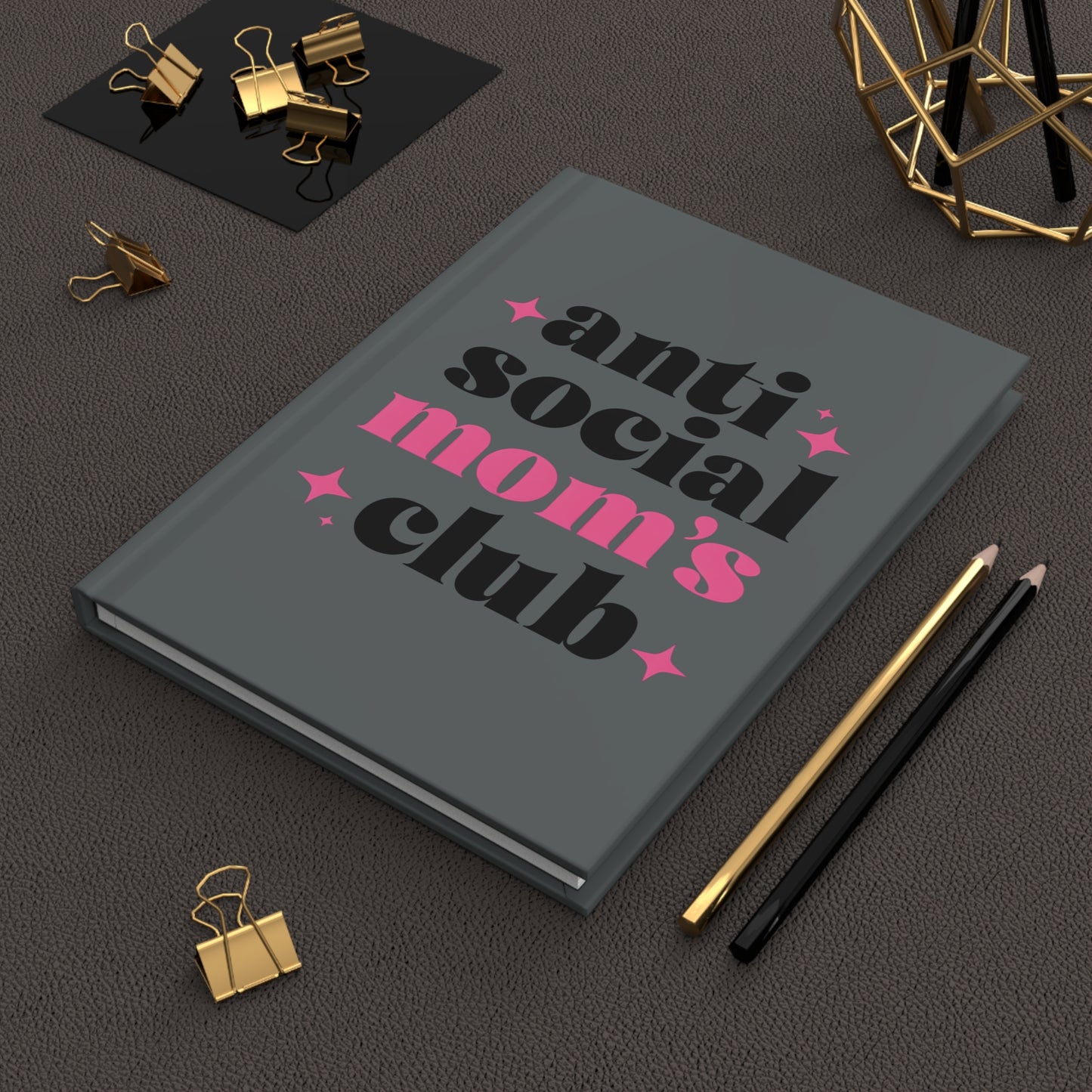 Gray hardcover journal with bold black and pink text that reads “anti social mom’s club” surrounded by pink star accents.