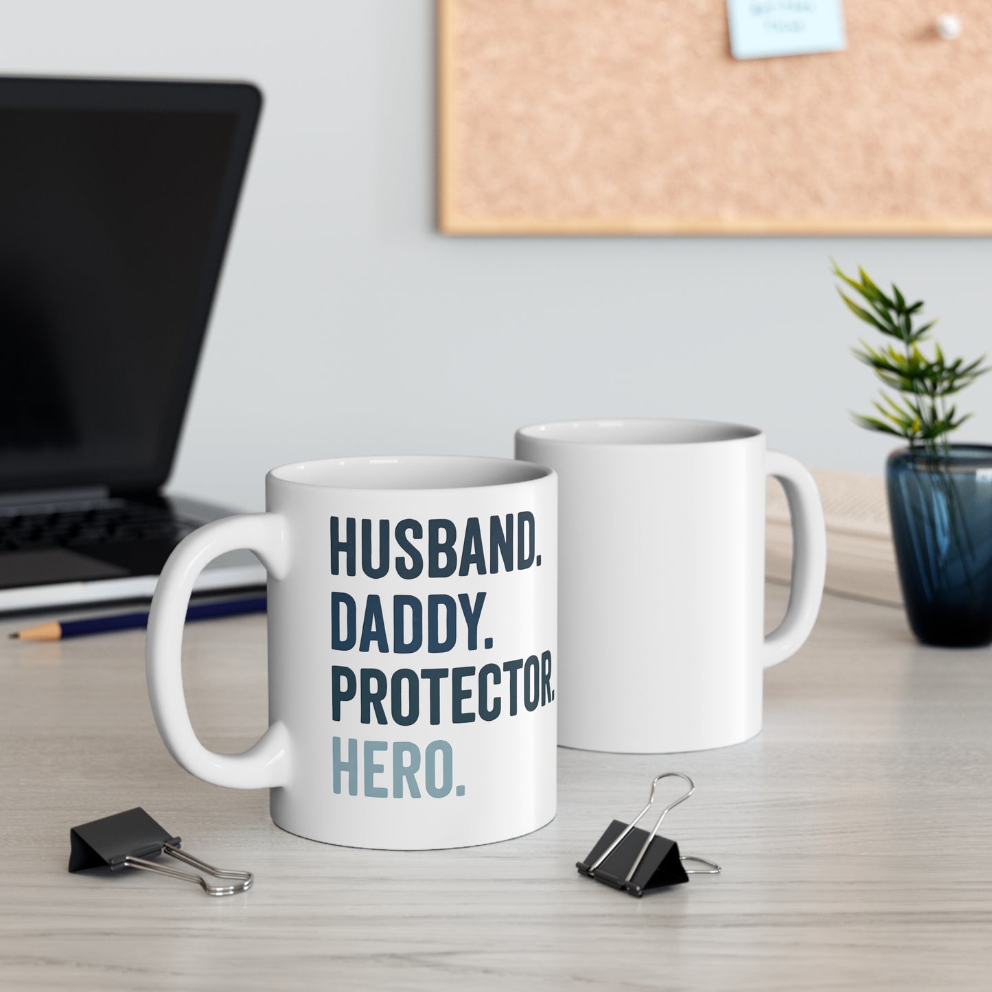 White ceramic mug with bold text reading "HUSBAND. DADDY. PROTECTOR. HERO." in navy and light blue.