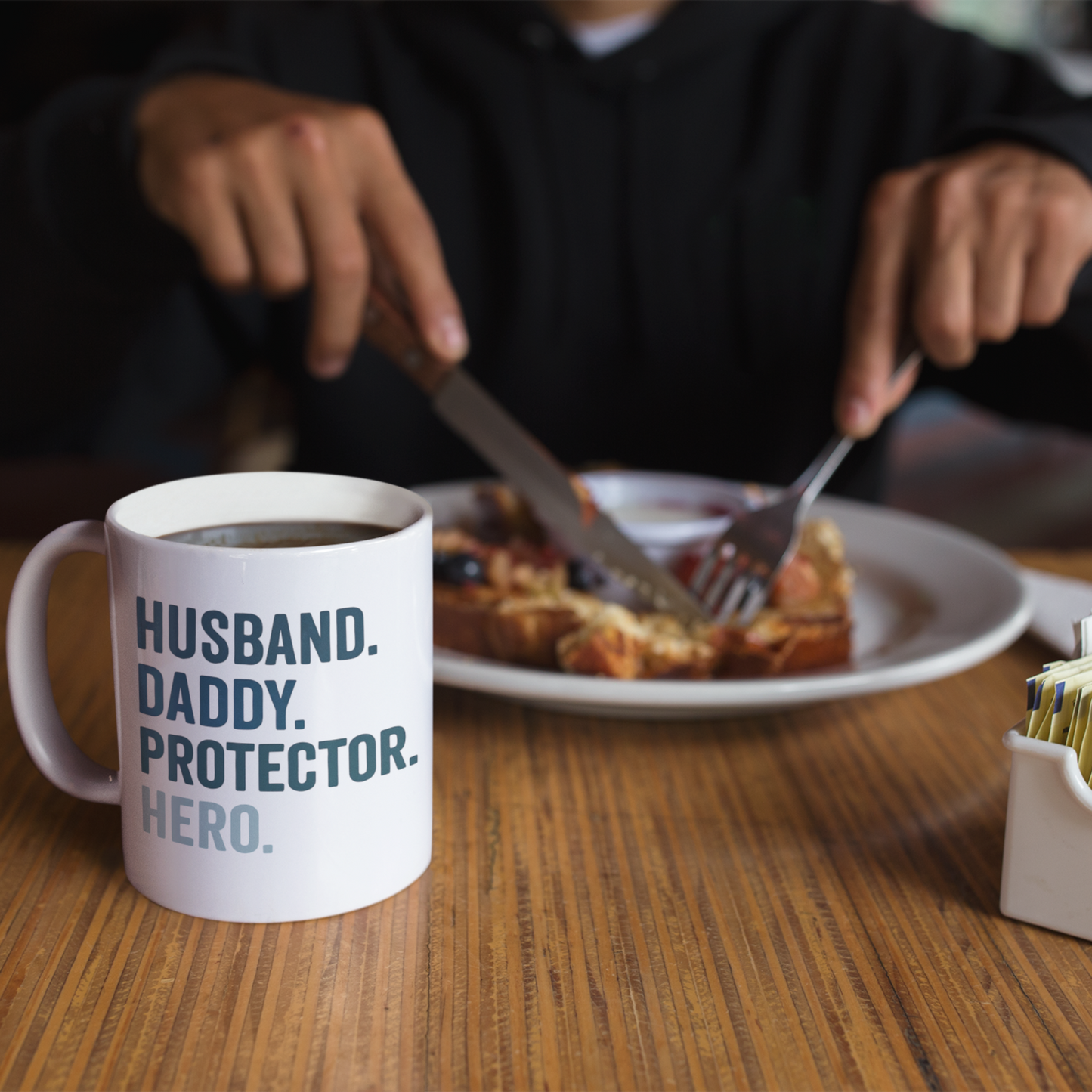 White ceramic mug with bold text reading "HUSBAND. DADDY. PROTECTOR. HERO." in navy and light blue.