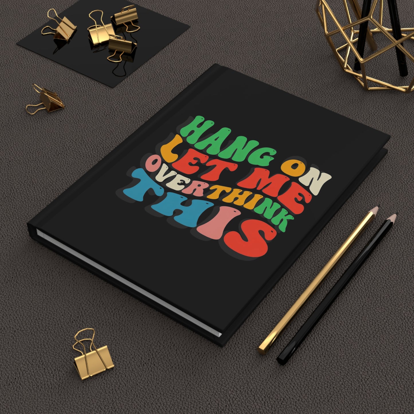 Hardcover journal with black cover featuring colorful retro-style text that reads “Hang On Let Me Overthink This” in bold, playful fonts.