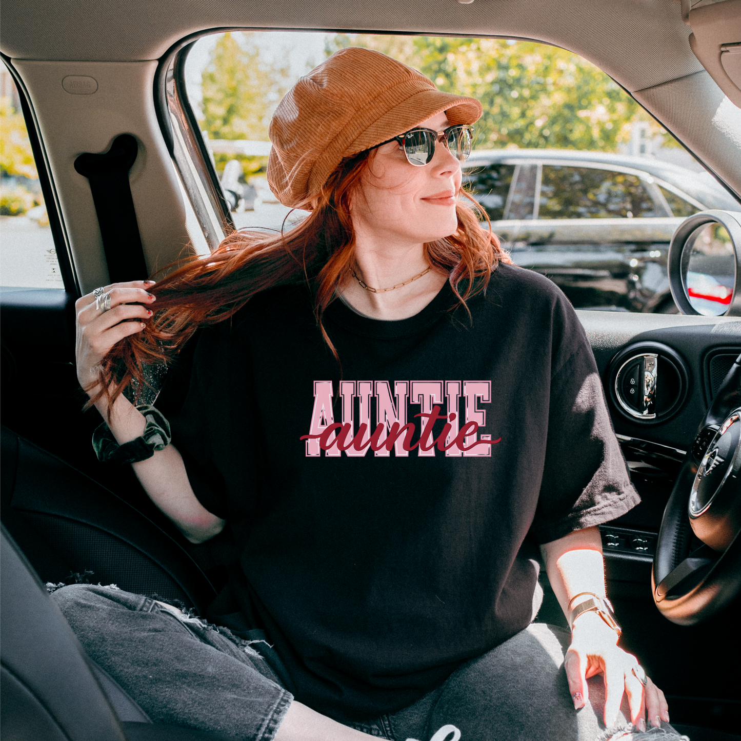 Women wearing graphic t-shirts with the word “AUNTIE” in bold pink varsity letters and a red cursive overlay, available in black, blue, green, and ivory, styled in lifestyle and casual settings
