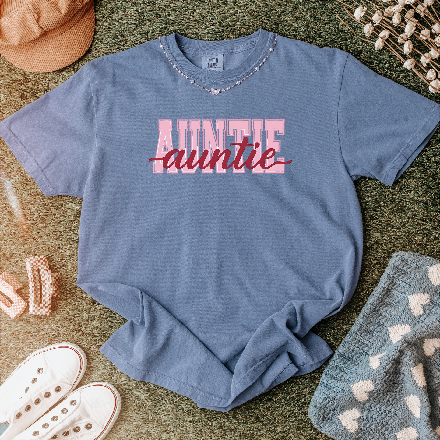 Women wearing graphic t-shirts with the word “AUNTIE” in bold pink varsity letters and a red cursive overlay, available in black, blue, green, and ivory, styled in lifestyle and casual settings
