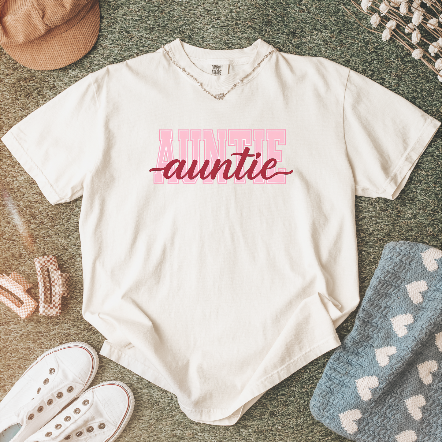 Women wearing graphic t-shirts with the word “AUNTIE” in bold pink varsity letters and a red cursive overlay, available in black, blue, green, and ivory, styled in lifestyle and casual settings