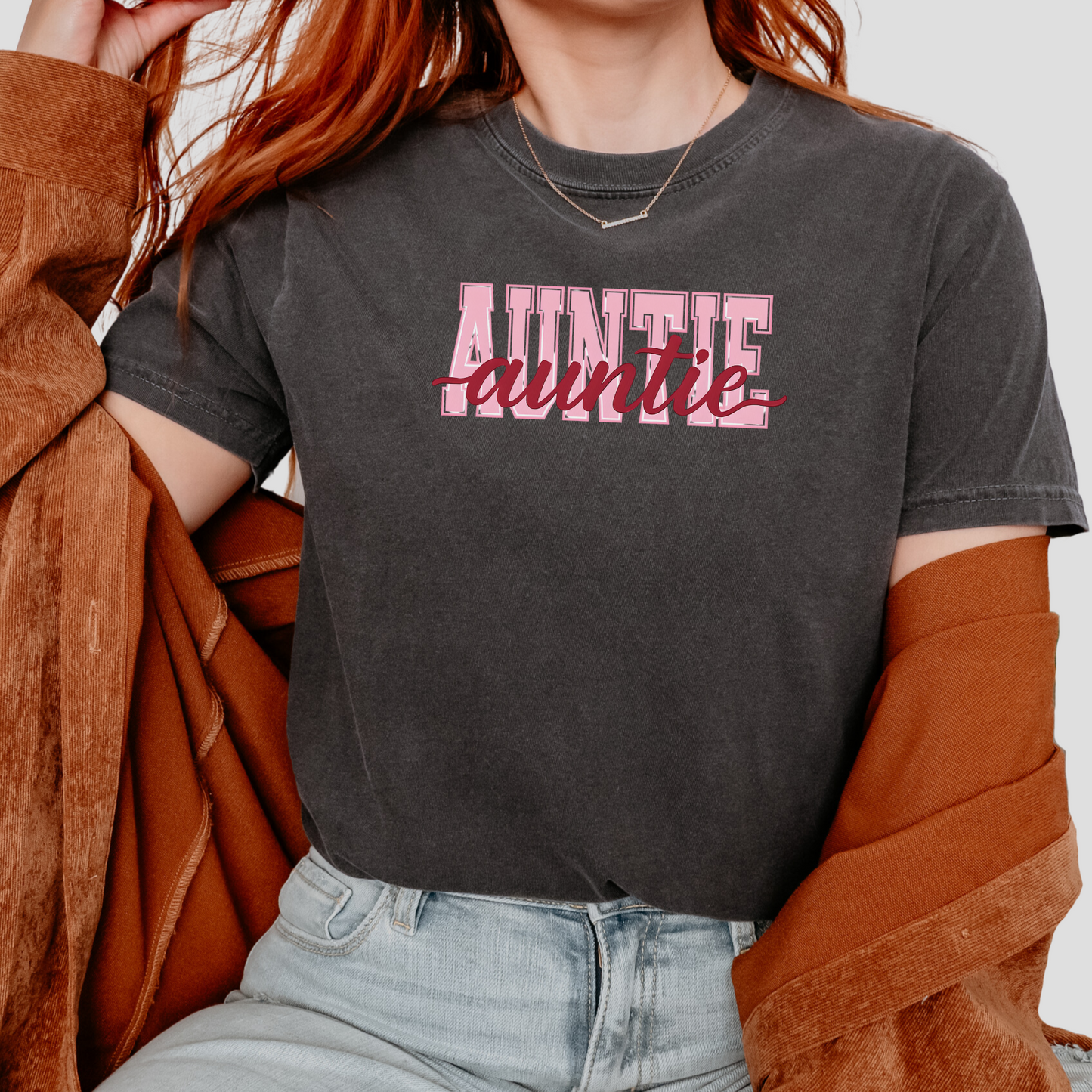 Women wearing graphic t-shirts with the word “AUNTIE” in bold pink varsity letters and a red cursive overlay, available in black, blue, green, and ivory, styled in lifestyle and casual settings