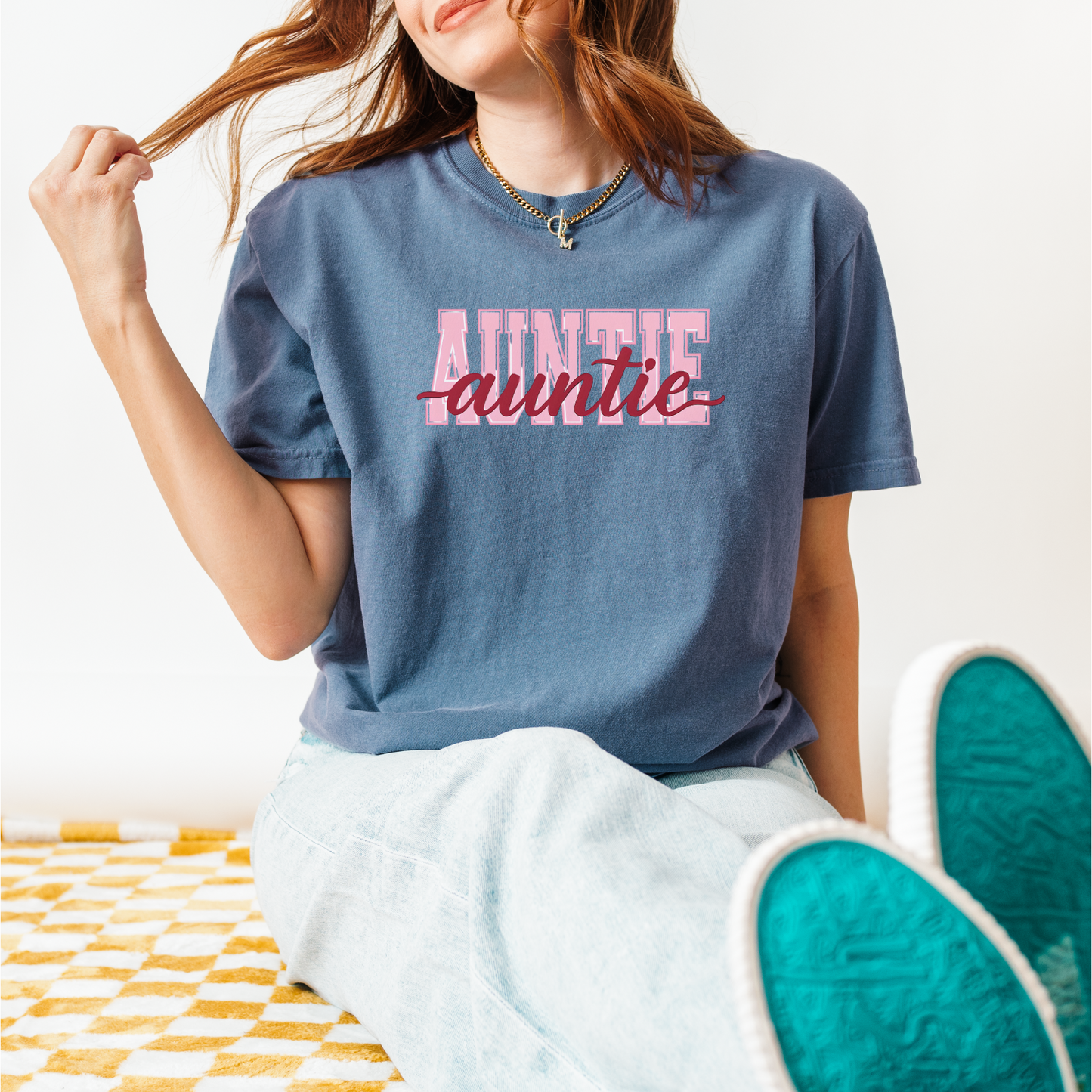 Women wearing graphic t-shirts with the word “AUNTIE” in bold pink varsity letters and a red cursive overlay, available in black, blue, green, and ivory, styled in lifestyle and casual settings