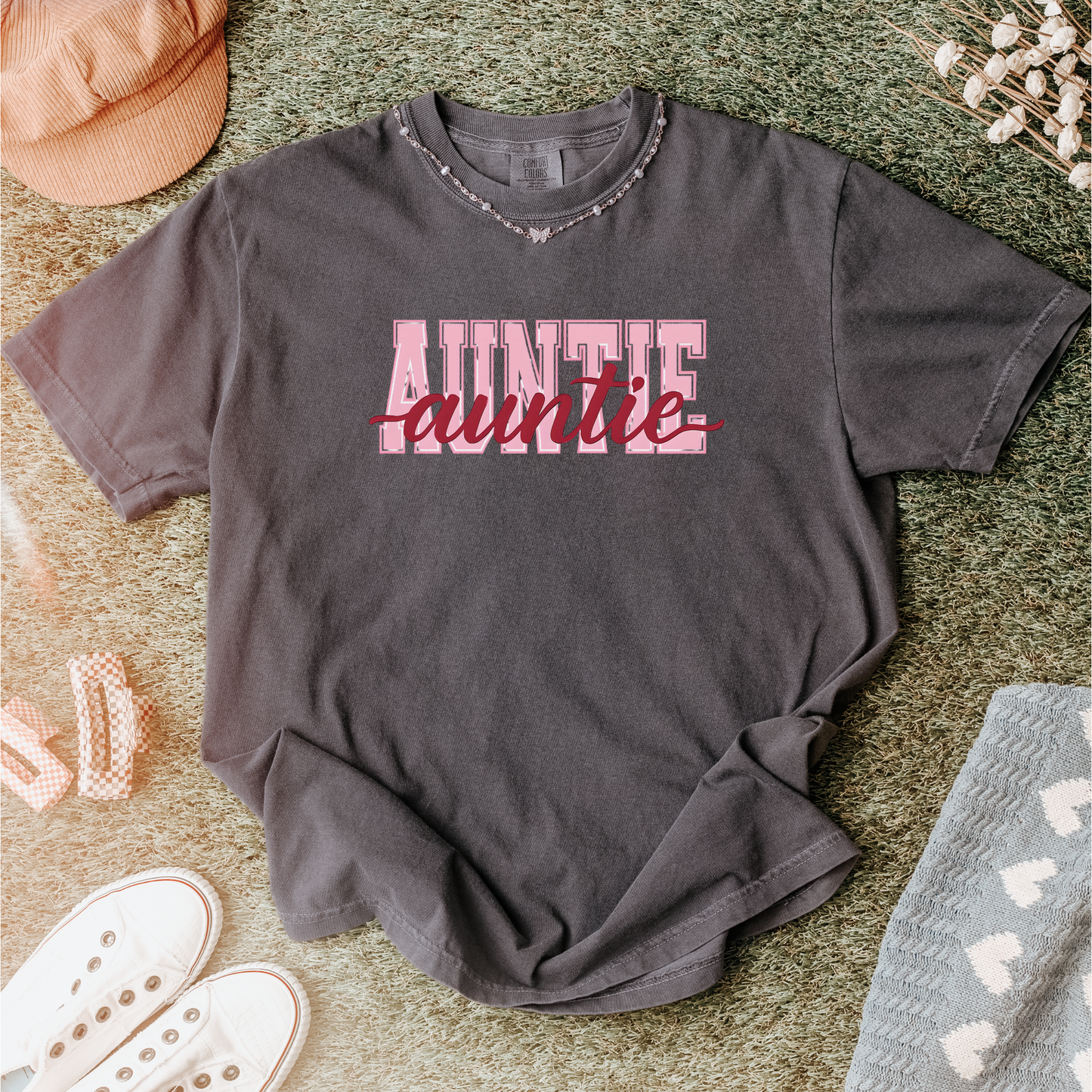 Women wearing graphic t-shirts with the word “AUNTIE” in bold pink varsity letters and a red cursive overlay, available in black, blue, green, and ivory, styled in lifestyle and casual settings
