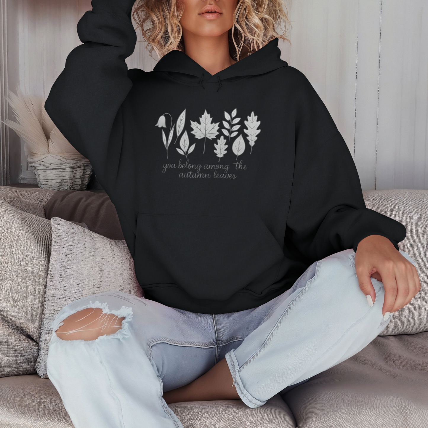 Person wearing a black hoodie with leaf design and text, sitting on a couch.