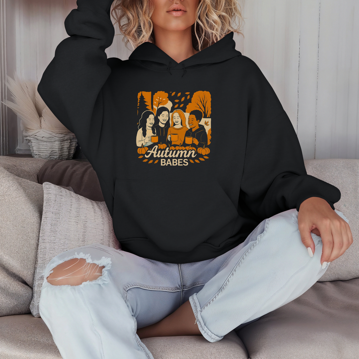 Person wearing a black hoodie with 'Autumn Babes' graphic sitting on a couch.