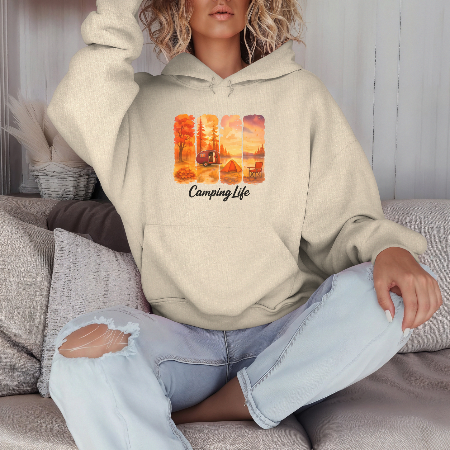 Person wearing a beige hoodie with 'Camping Life' design sitting on a couch.