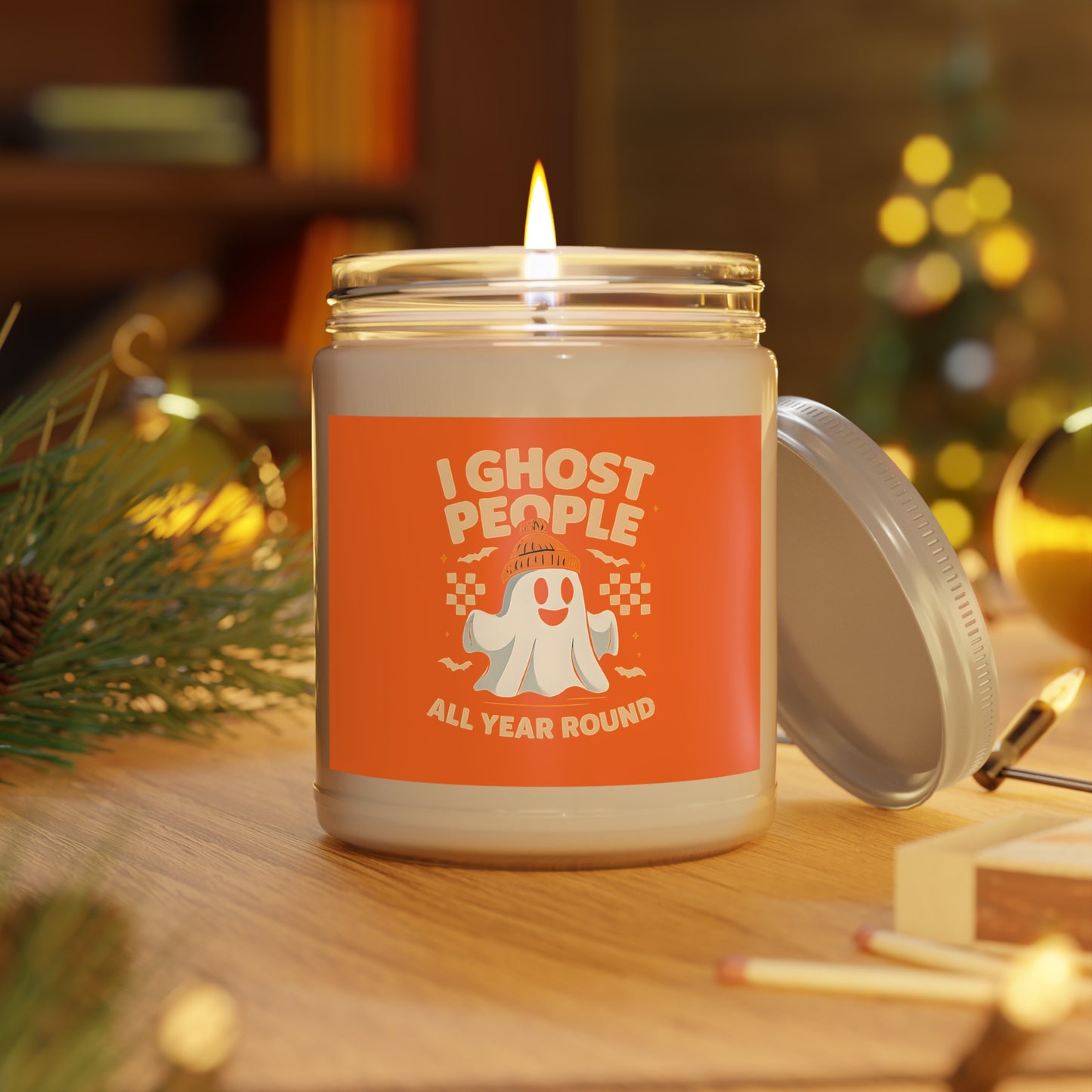 Candle in a jar with a ghost-themed label on a wooden surface with festive decorations.