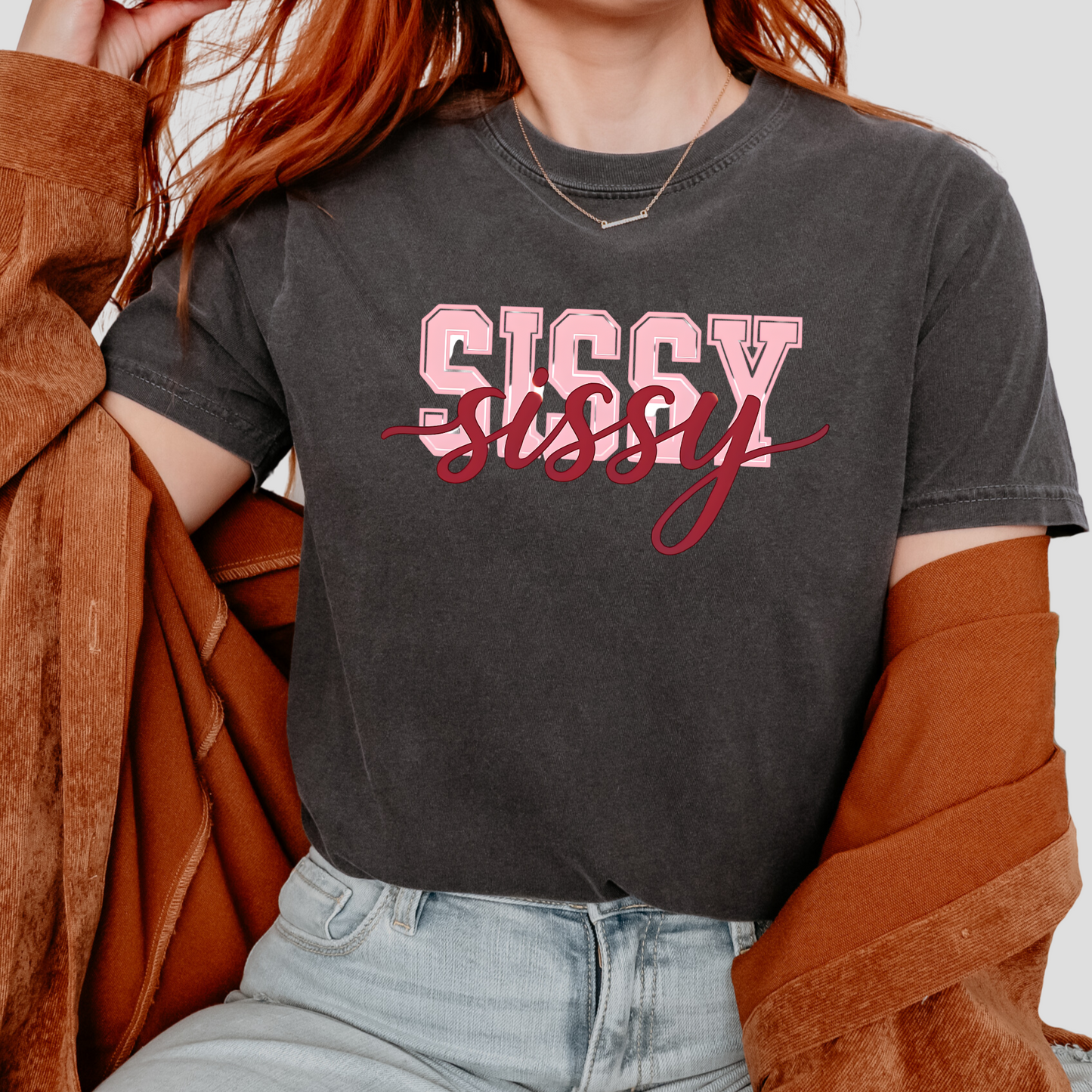 Women wearing t-shirts with the word “SISSY” in pink varsity letters overlaid with dark red cursive script, in colors including charcoal, denim blue, green, black, and ivory, styled in casual everyday scenes