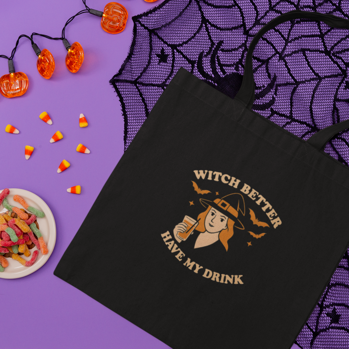 Black tote bag with Halloween-themed design on a purple background with candy and lights.
