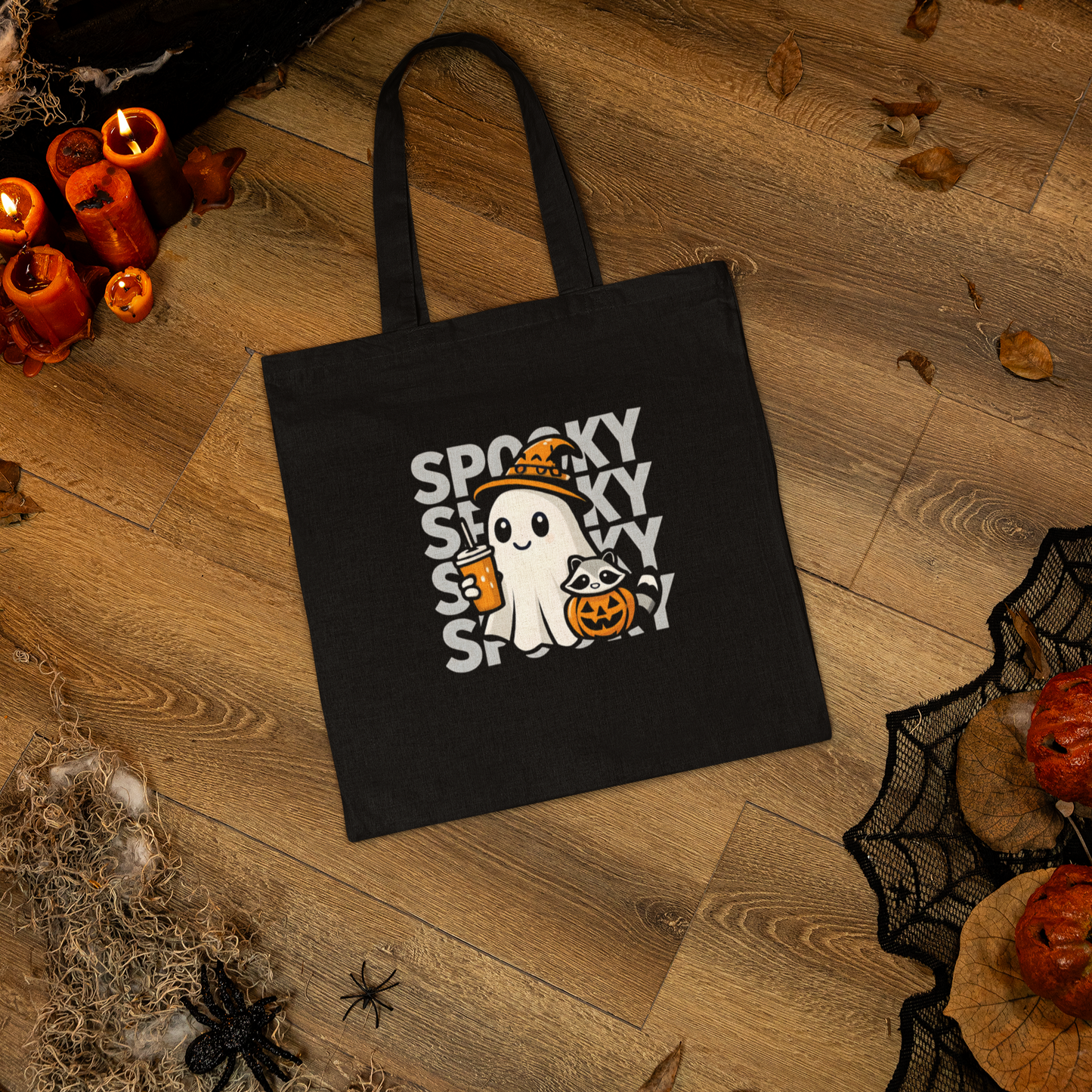 Black tote bag with Halloween design featuring a ghost and text on a wooden floor.