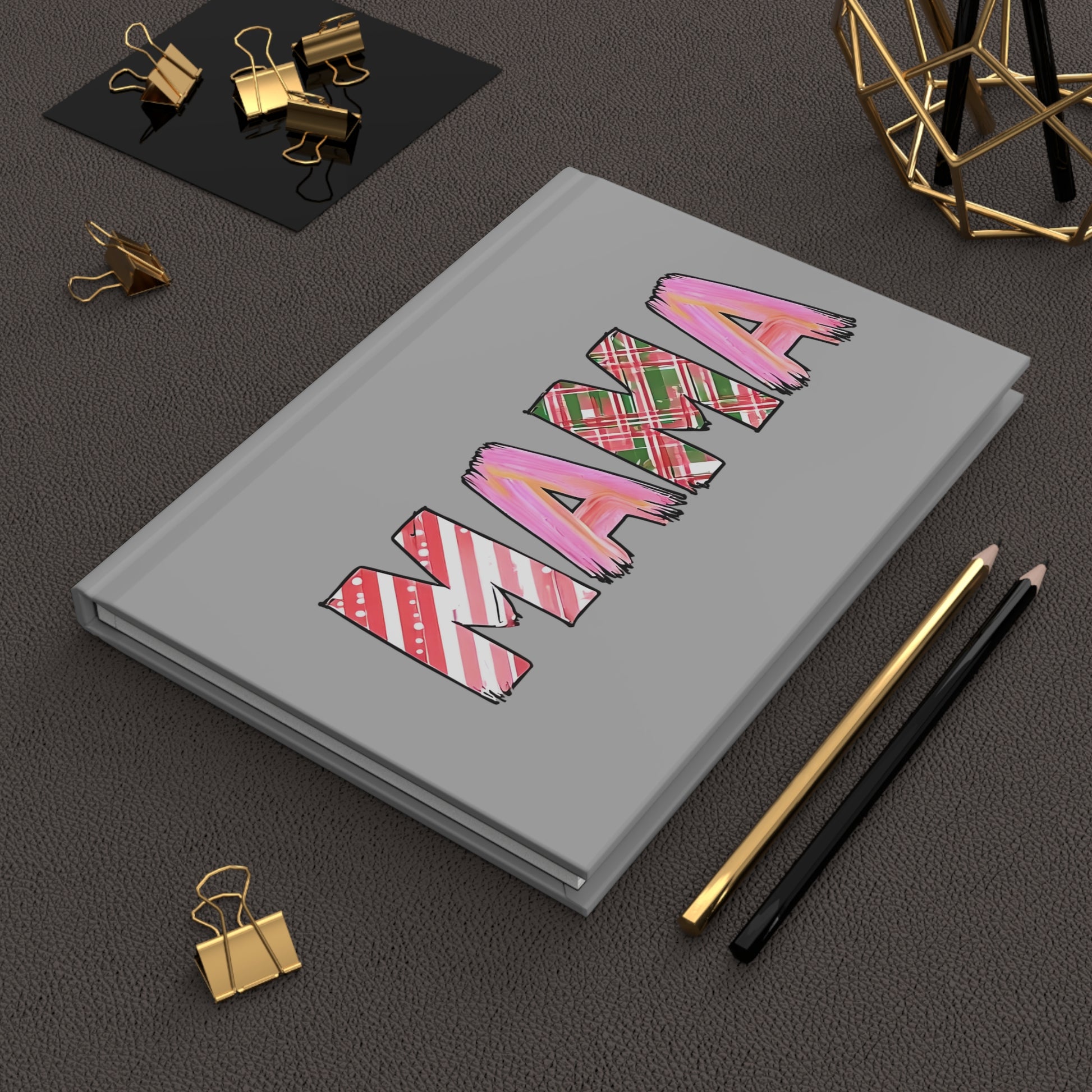 Gray hardcover journal with the word “MAMA” in large letters, each filled with holiday-themed patterns including pink brushstrokes, red and green plaid, and candy cane stripes.