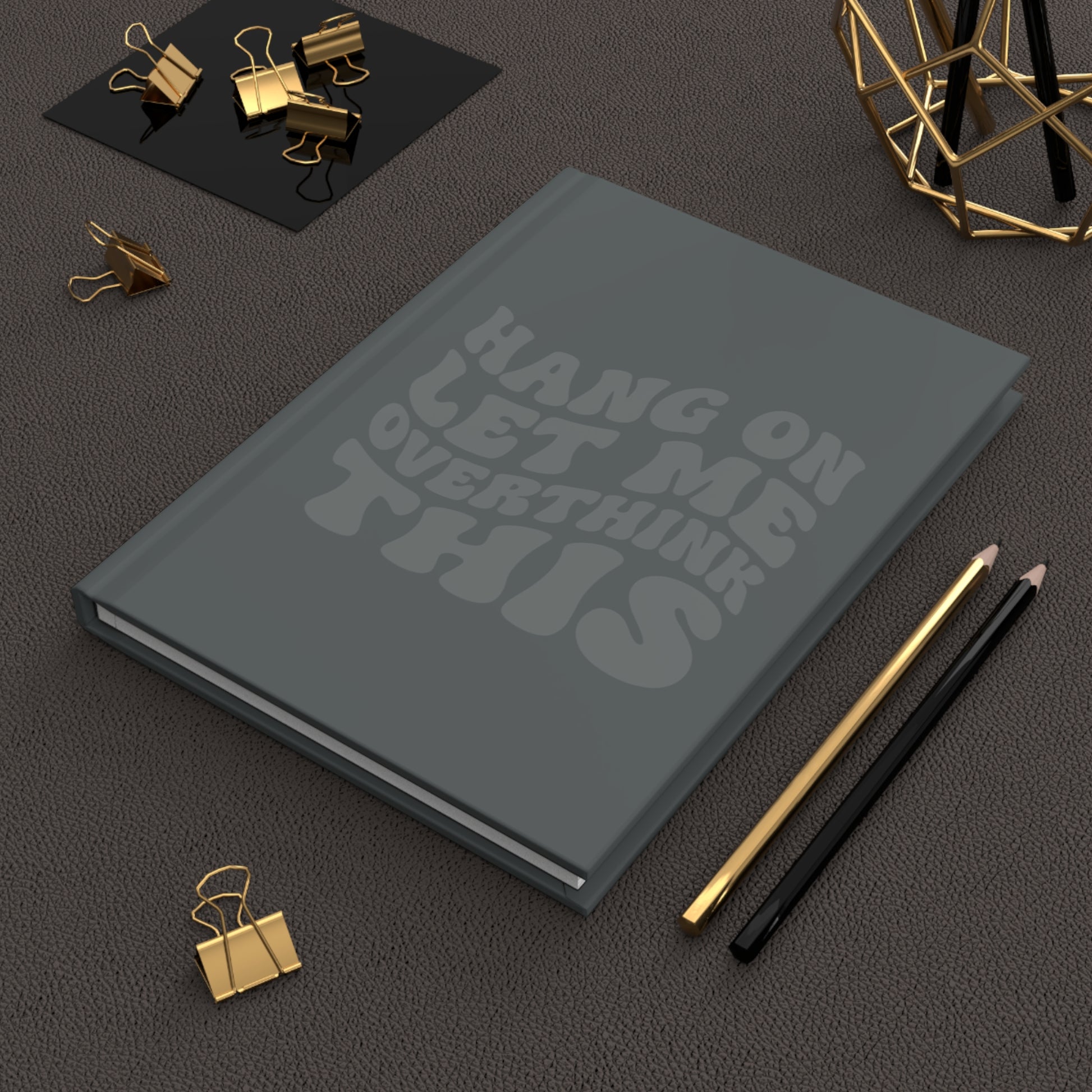 Gray hardcover journal with dark gray retro-style text that reads “Hang On Let Me Overthink This” in a monochrome design.