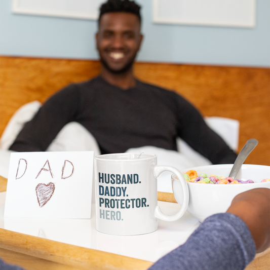 White ceramic mug with bold text reading "HUSBAND. DADDY. PROTECTOR. HERO." in navy and light blue.