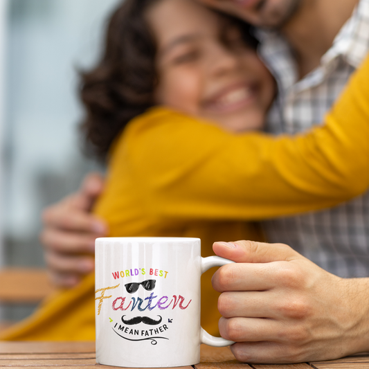 White ceramic mug with colorful text saying “World’s Best Farter I Mean Father,” featuring playful fonts, sunglasses, and a mustache graphic.