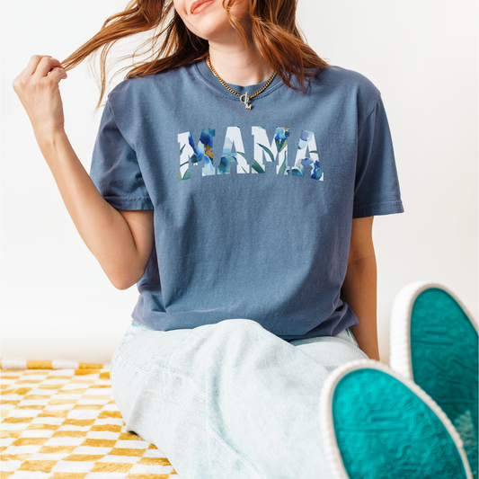 T-shirt featuring the word “MAMA” in large blue floral lettering, shown in black, slate blue, sage green, charcoal, and soft yellow color variations