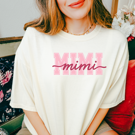 T-shirts with “MIMI” in large pink varsity letters and cursive “mimi” overlay in script, shown in black, blue, sage green, charcoal, and ivory colorways with styled flat-lay backgrounds