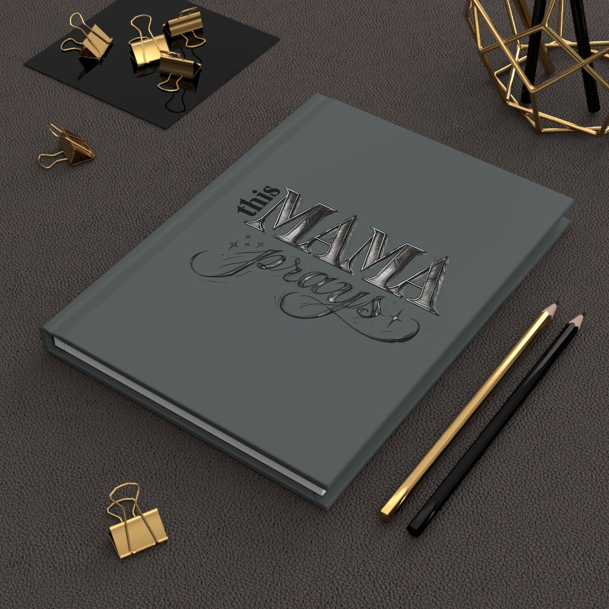 Gray hardcover journal with elegant silver-gray text that reads “This Mama Prays” in decorative fonts with subtle stars and swirls.