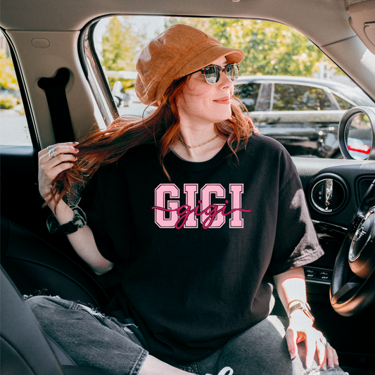 Women wearing soft cotton t-shirts with “GIGI” in bold pink varsity block letters and cursive red script, shown in various lifestyle scenes and color options including black, blue, sage, and ivory