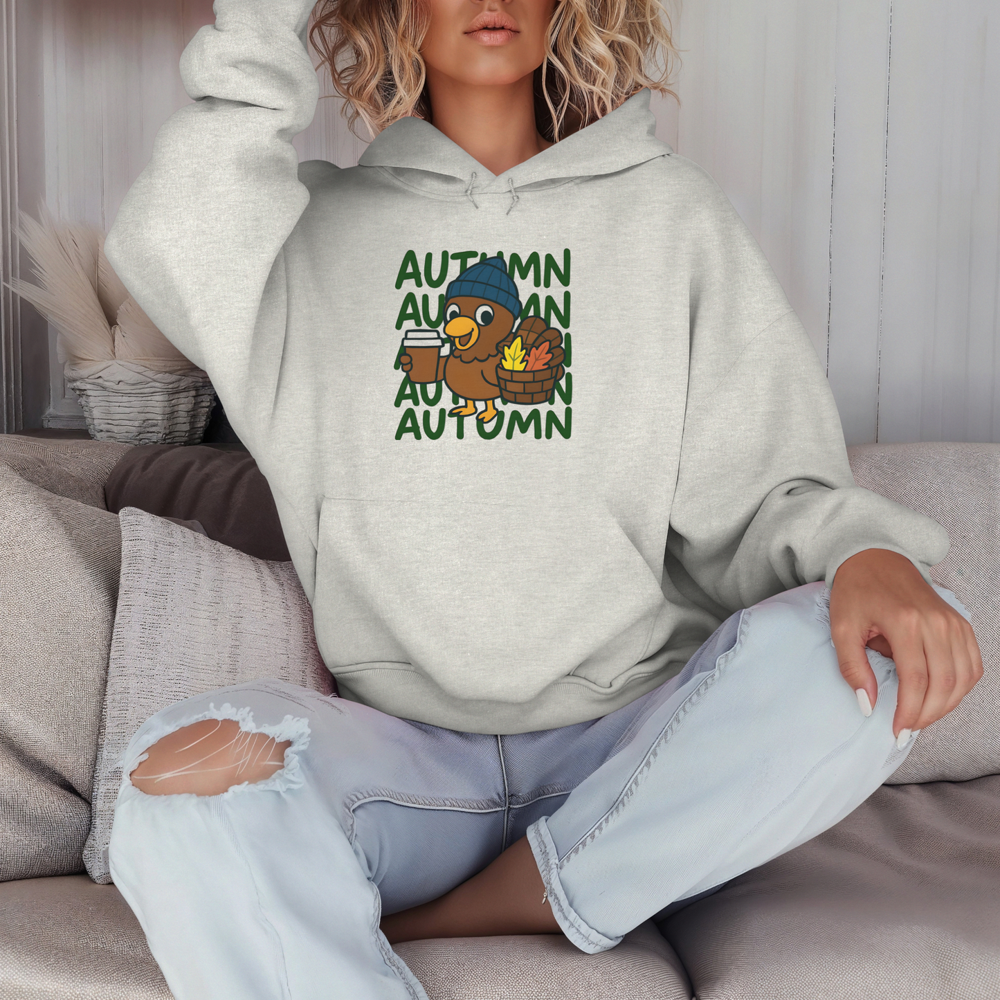 Person wearing a light gray hoodie with autumn-themed design sitting on a couch.