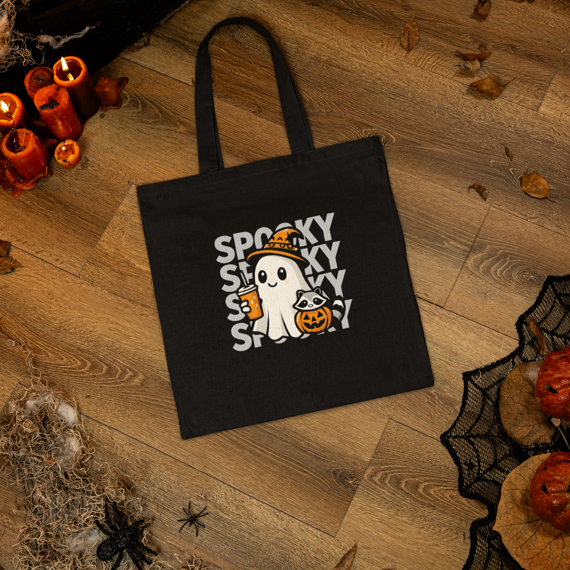 Black tote bag with Halloween design featuring a ghost and text on a wooden floor.